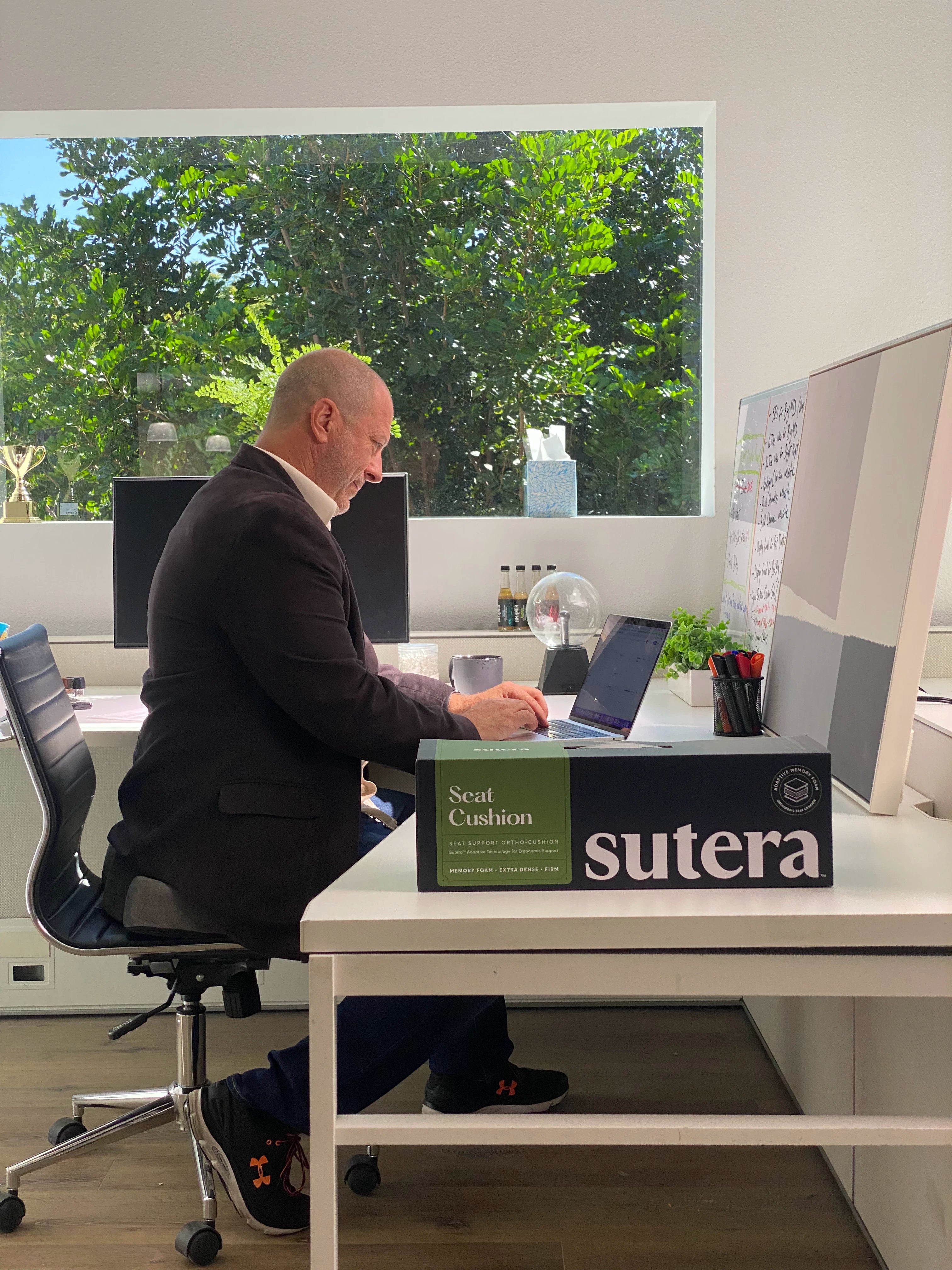 Happy man at work sitting in a chair with good posture using the ortho seat cushion from Sutera.